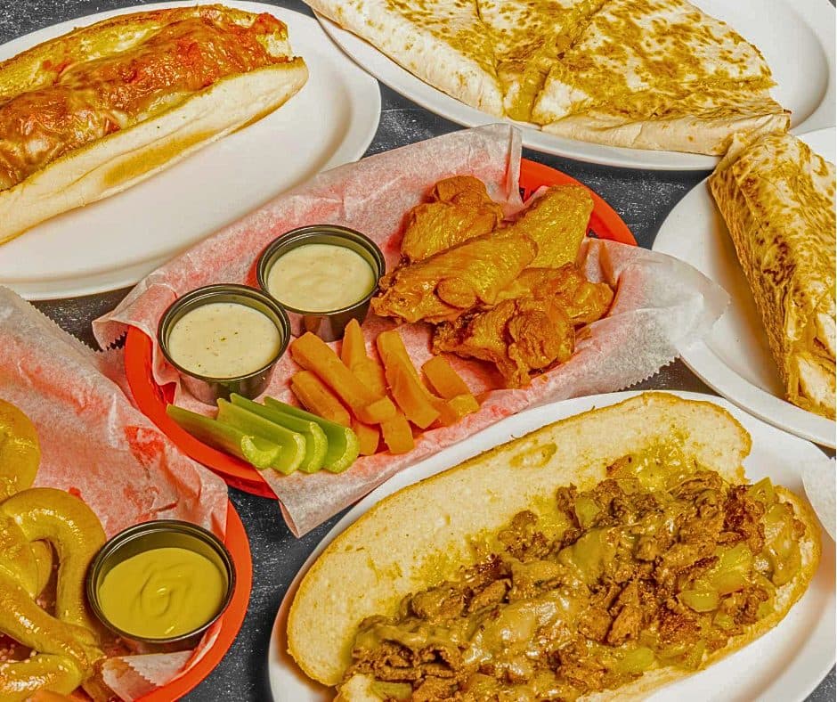 A spread of Play By Play food including wings, a pretzel, a quesadilla and a Philly cheesesteak